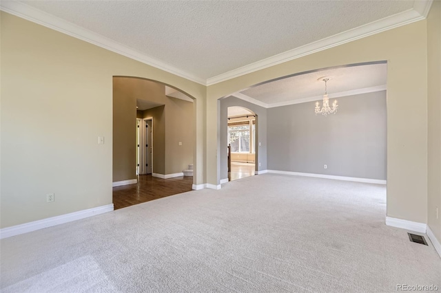 carpeted spare room featuring arched walkways, a textured ceiling, ornamental molding, a chandelier, and baseboards