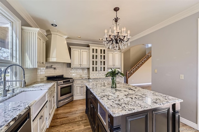 kitchen featuring glass insert cabinets, tasteful backsplash, wall chimney range hood, appliances with stainless steel finishes, and cream cabinets