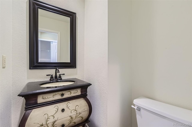 half bathroom with a textured wall, vanity, and toilet