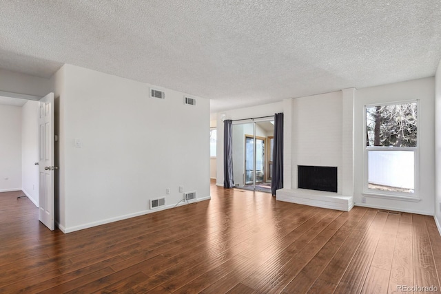 unfurnished living room with dark wood-type flooring, a brick fireplace, and a textured ceiling