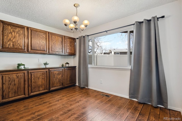 unfurnished dining area with dark hardwood / wood-style floors, an inviting chandelier, and a textured ceiling