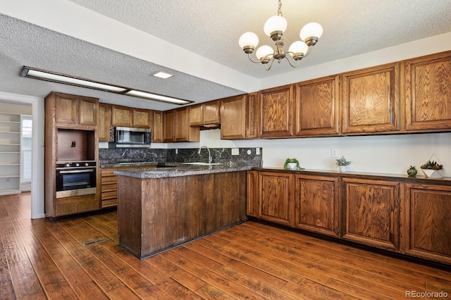 kitchen with sink, an inviting chandelier, dark hardwood / wood-style floors, pendant lighting, and stainless steel appliances