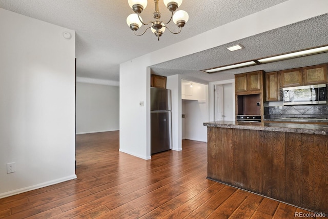 kitchen with appliances with stainless steel finishes, an inviting chandelier, hanging light fixtures, a textured ceiling, and dark hardwood / wood-style flooring