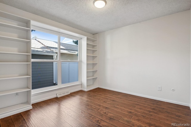 unfurnished room with dark wood-type flooring, built in features, and a textured ceiling