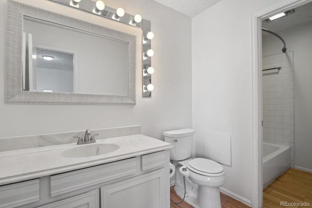 full bathroom with hardwood / wood-style flooring, tiled shower / bath combo, vanity, a textured ceiling, and toilet