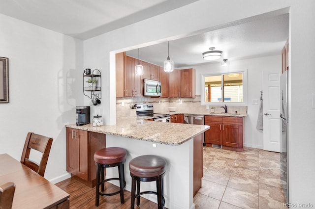 250 W Midway Blvd, Broomfield, CO 80020 - kitchen featuring appliances with stainless steel finishes, a peninsula, backsplash, a kitchen breakfast bar, and brown cabinets