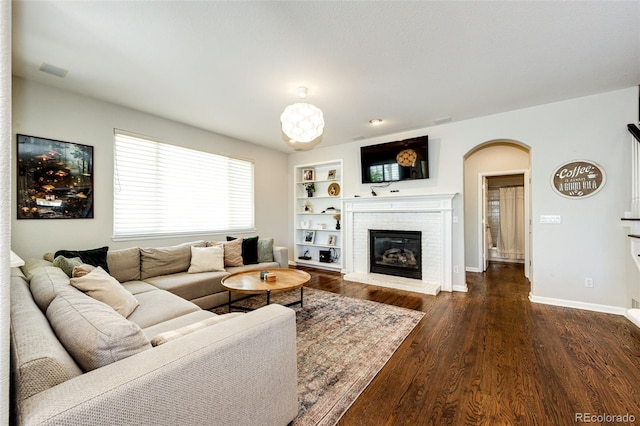4970 Laurelglen Ln, Highlands Ranch, CO 80130 - living area featuring arched walkways, a brick fireplace, built in features, dark wood-style flooring, and baseboards