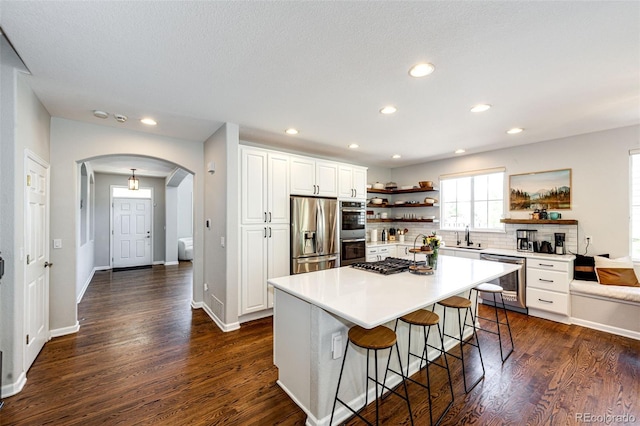 4970 Laurelglen Ln, Highlands Ranch, CO 80130 - kitchen featuring open shelves, stainless steel appliances, arched walkways, dark wood-style floors, and a breakfast bar