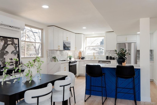 kitchen featuring appliances with stainless steel finishes, a breakfast bar area, a wall mounted air conditioner, light countertops, and white cabinetry