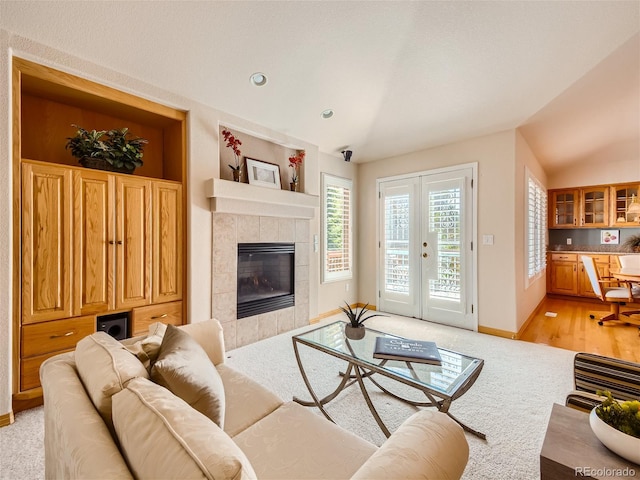 living room featuring a tiled fireplace, light carpet, french doors, and lofted ceiling