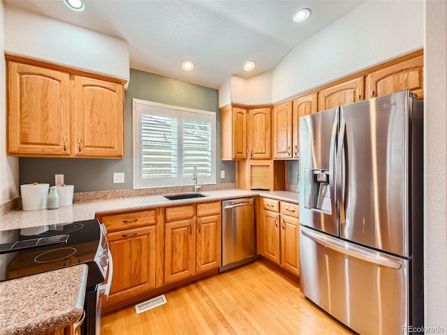 kitchen featuring sink, stainless steel appliances, vaulted ceiling, and light hardwood / wood-style floors