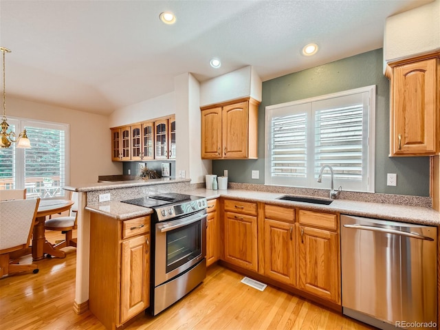 kitchen with kitchen peninsula, appliances with stainless steel finishes, sink, an inviting chandelier, and hanging light fixtures