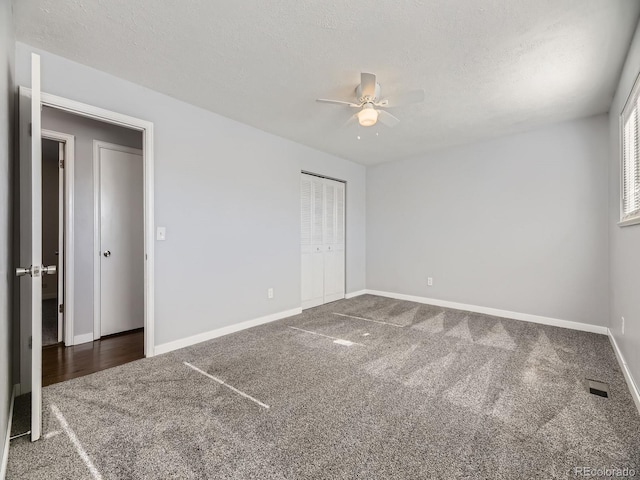 unfurnished bedroom featuring dark carpet, a textured ceiling, a closet, and ceiling fan