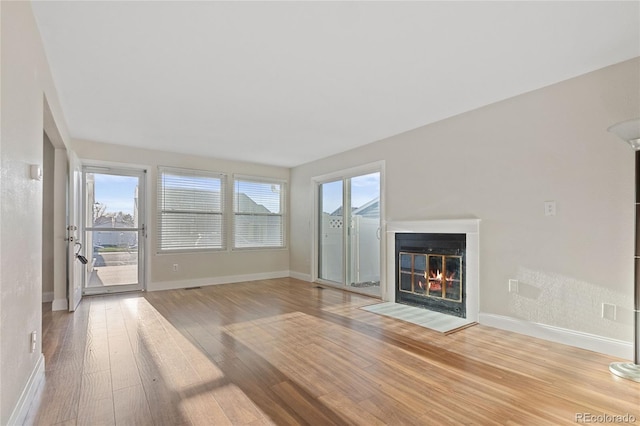 unfurnished living room with a fireplace with flush hearth, wood finished floors, and baseboards
