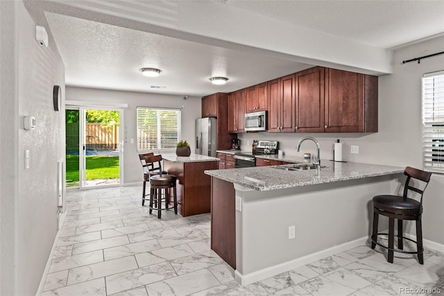 18672 E Chaffee Pl, Denver, CO 80249 - kitchen featuring appliances with stainless steel finishes, light marble finish floors, a kitchen bar, plenty of natural light, and a textured ceiling