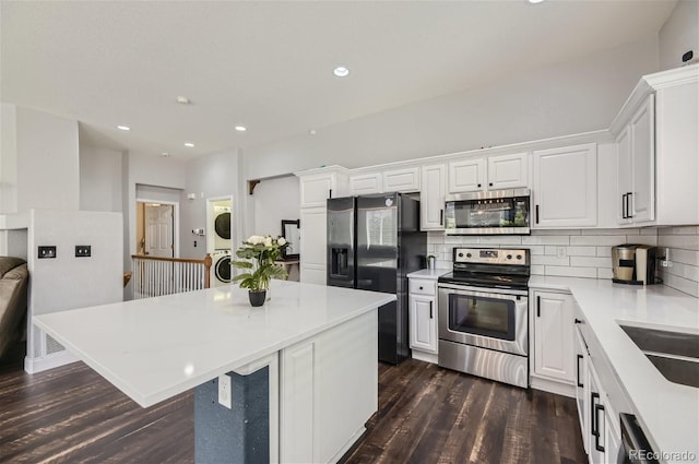 kitchen with stainless steel appliances, a kitchen island, stacked washer and dryer, white cabinets, and dark wood-type flooring