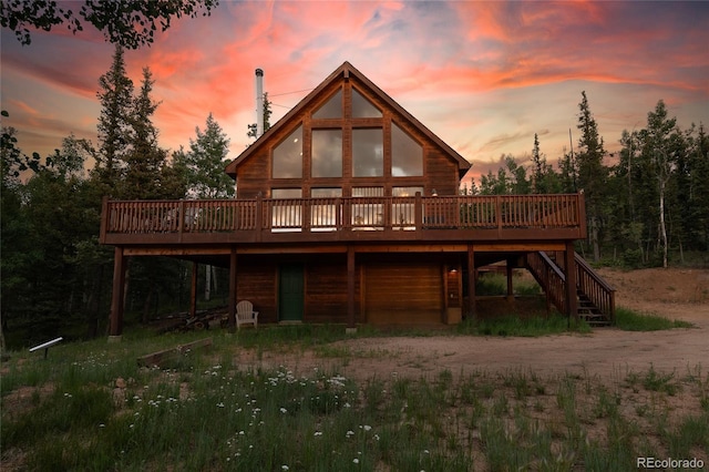 back of house at dusk featuring stairway, driveway, and a wooden deck