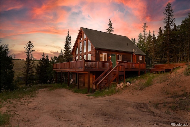 back of house at dusk with a wooden deck, stairs, and driveway