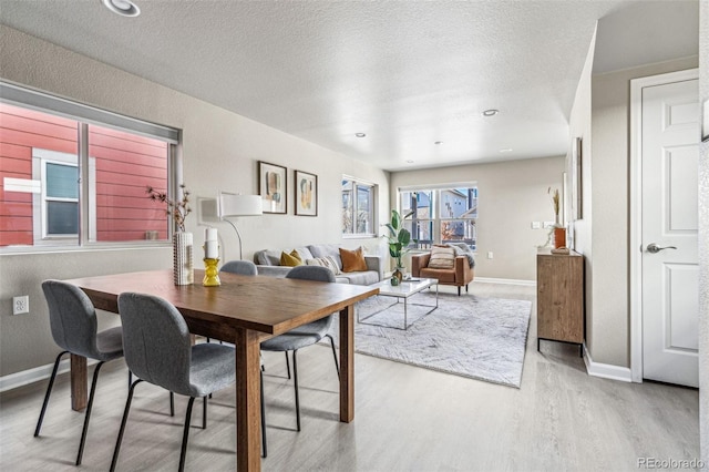 dining space featuring light wood-type flooring, a textured ceiling, and baseboards