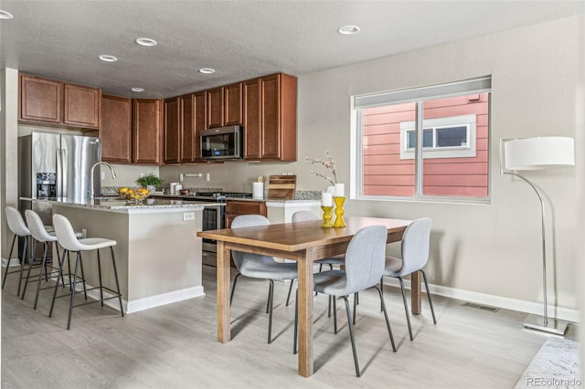 kitchen with a textured ceiling, stainless steel appliances, visible vents, a kitchen breakfast bar, and light wood-type flooring