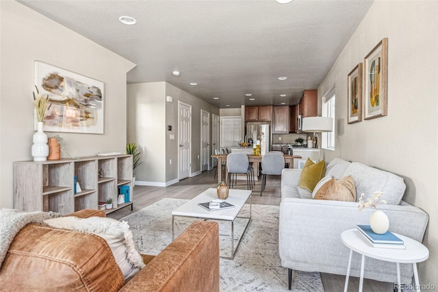 living area featuring light wood-style flooring, baseboards, a textured ceiling, and recessed lighting