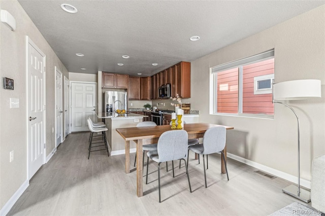 dining room with baseboards, a textured ceiling, recessed lighting, and light wood-style floors