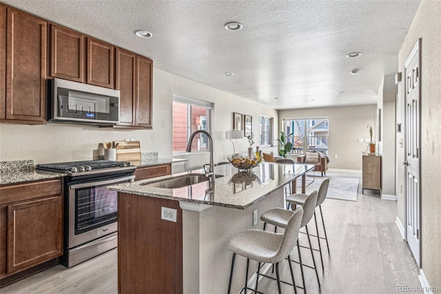 kitchen featuring appliances with stainless steel finishes, light wood-type flooring, a sink, and a kitchen bar