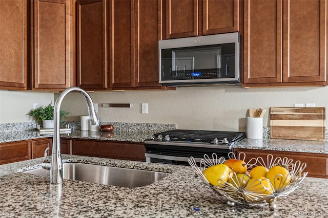 kitchen featuring appliances with stainless steel finishes, light stone counters, and a sink