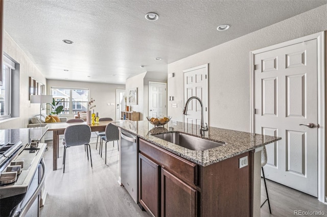 kitchen featuring light wood-style flooring, open floor plan, a sink, dishwasher, and a kitchen bar