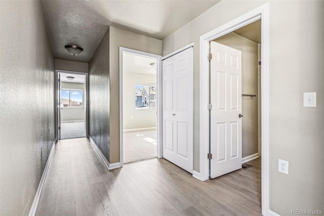 corridor with a textured ceiling, baseboards, wood finished floors, and a textured wall