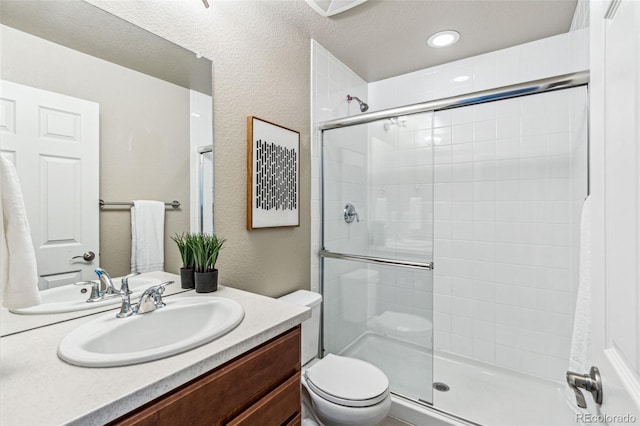 bathroom with a textured wall, tiled shower, vanity, and toilet