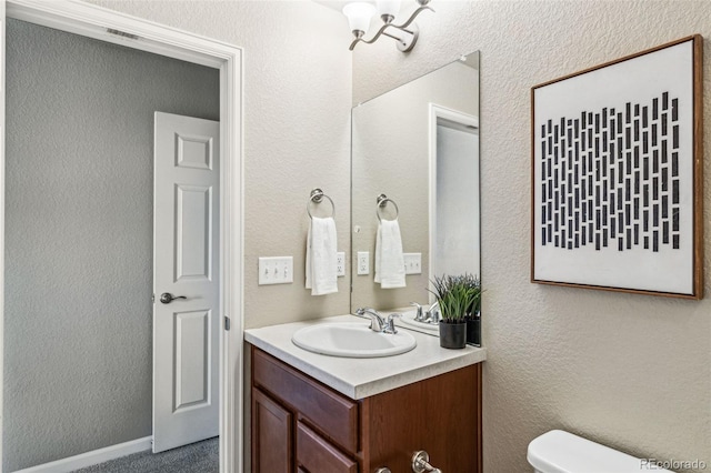 half bathroom featuring toilet, a textured wall, visible vents, and vanity