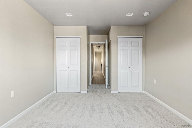 unfurnished bedroom featuring carpet, baseboards, and two closets