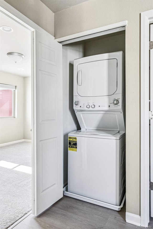 laundry area featuring laundry area, baseboards, stacked washing maching and dryer, and wood finished floors