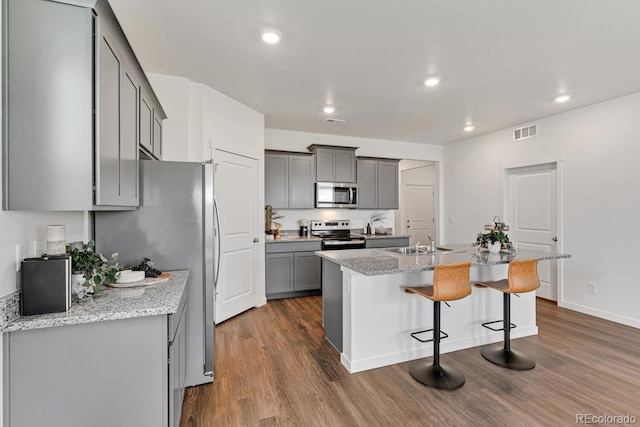 kitchen with visible vents, gray cabinetry, dark wood-type flooring, appliances with stainless steel finishes, and a kitchen breakfast bar