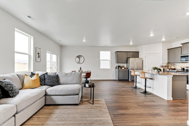 living room with recessed lighting, visible vents, plenty of natural light, and dark wood-type flooring