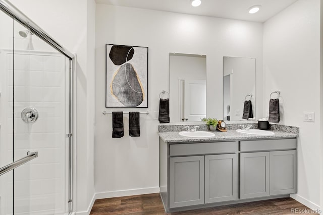 full bath with baseboards, double vanity, a stall shower, wood finished floors, and a sink