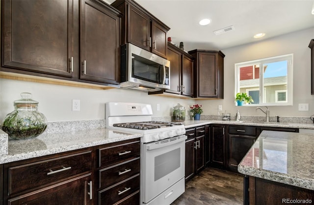 kitchen featuring stainless steel microwave, light stone counters, white gas range oven, dark wood-style floors, and visible vents