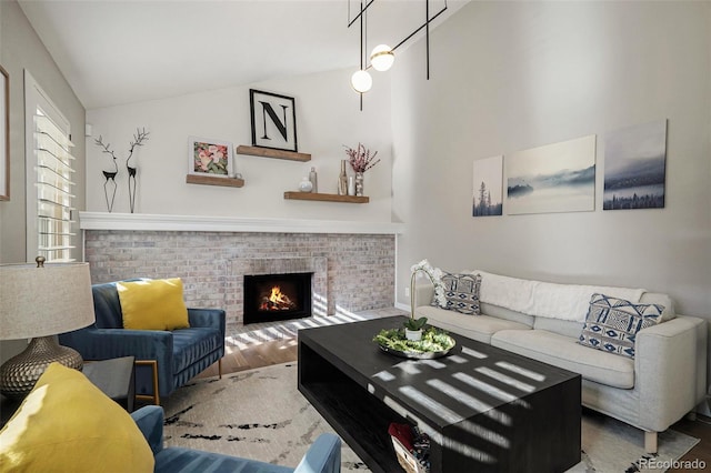 living room featuring vaulted ceiling, a brick fireplace, and wood finished floors