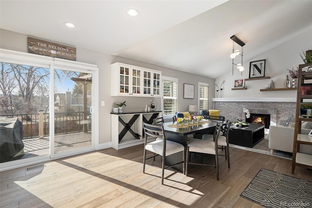 dining room with visible vents, wood finished floors, recessed lighting, a fireplace, and vaulted ceiling