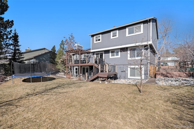 rear view of property featuring a trampoline, a wooden deck, stairs, a lawn, and a pergola