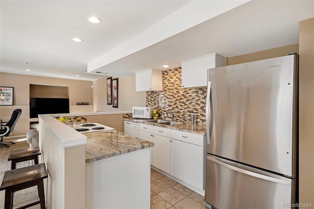 kitchen featuring a breakfast bar, a sink, white cabinetry, white appliances, and decorative backsplash