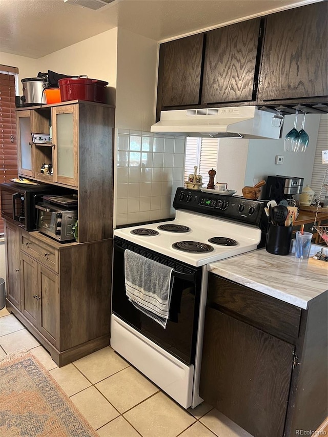 kitchen featuring light tile patterned flooring, a toaster, under cabinet range hood, light countertops, and electric range