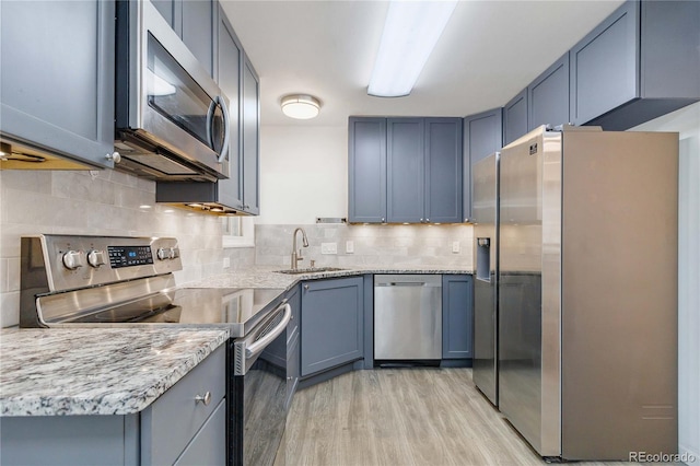 kitchen with sink, light hardwood / wood-style flooring, appliances with stainless steel finishes, light stone counters, and decorative backsplash