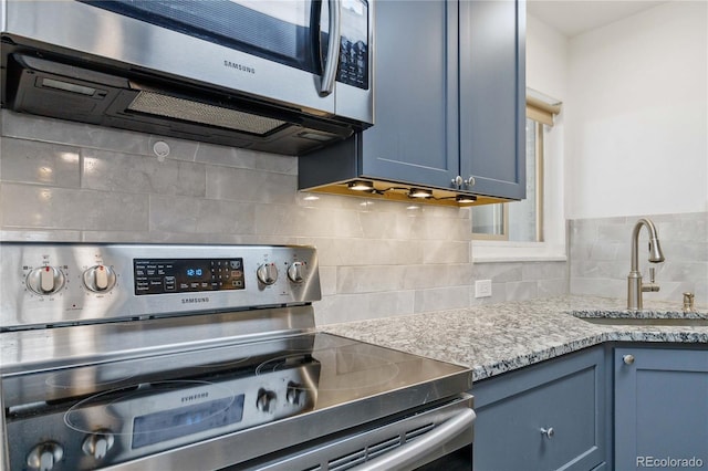 kitchen with stainless steel appliances, blue cabinets, sink, and decorative backsplash