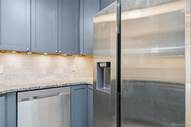 kitchen with stainless steel appliances, light stone countertops, blue cabinetry, and backsplash