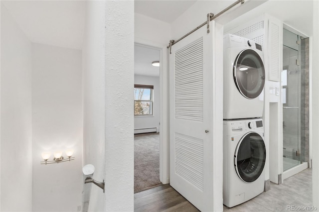 washroom with a baseboard radiator, stacked washer and clothes dryer, and light wood-type flooring