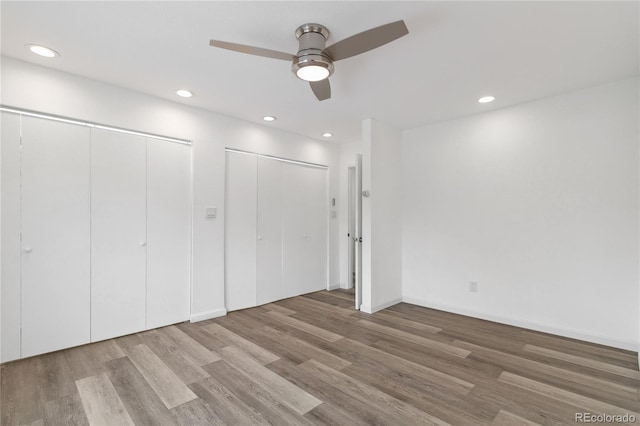 unfurnished bedroom with ceiling fan, hardwood / wood-style floors, and two closets