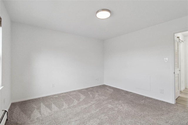 carpeted empty room featuring a baseboard heating unit