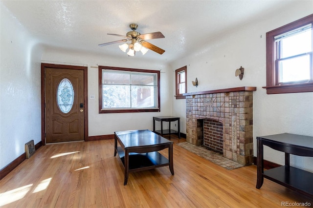 living room with ceiling fan, light hardwood / wood-style floors, a textured ceiling, and a fireplace